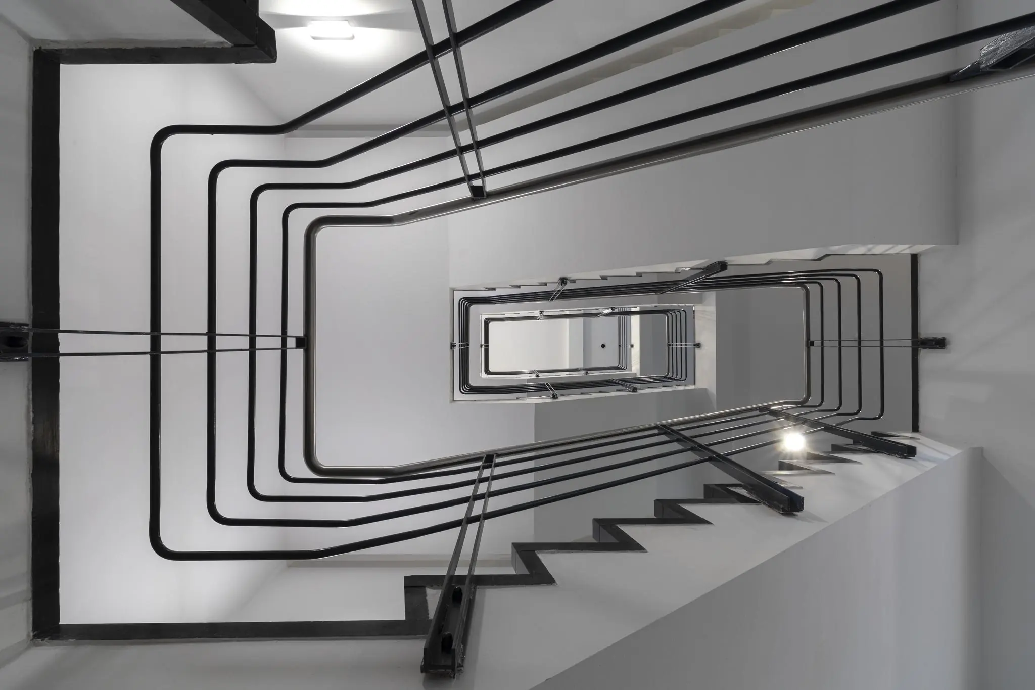 Doorkijk vanaf beneden in het trappenhuis van een modern appartementencomplex aan de Van Boshuizenstraat met geometrische zwarte leuningen.